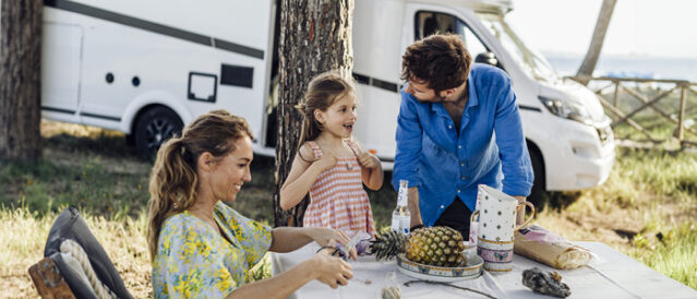 Nærbilde av familie som koser seg i naturen med bobil i bakgrunnen